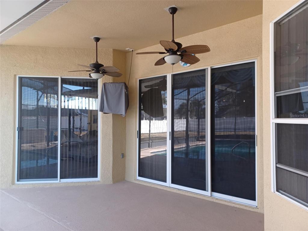 A covered patio features two ceiling fans, sliding glass doors, and a view of a pool — 3513 BEAU CHENE DRIVE, KISSIMMEE, FL