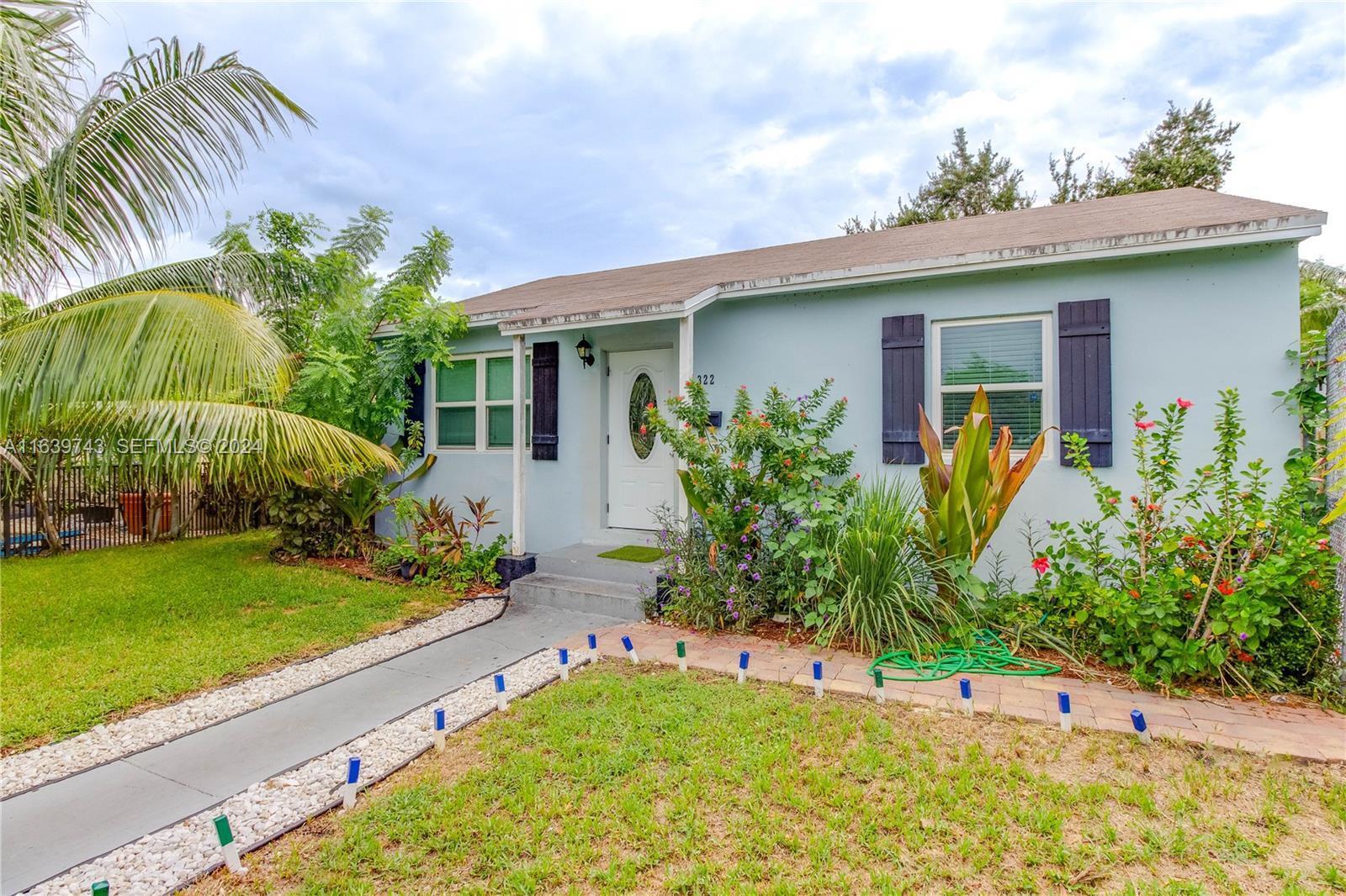 A light blue single-story house features dark shutters, a white front door, and landscaped gardens — 322 N C Street, FL 33460, FL