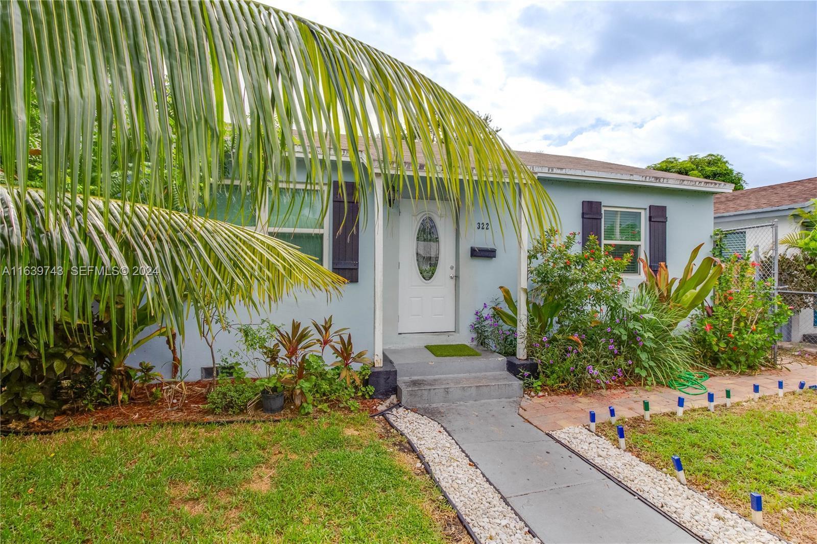A light blue single-story house features a white front door and a palm tree — 322 N C Street, FL 33460, FL