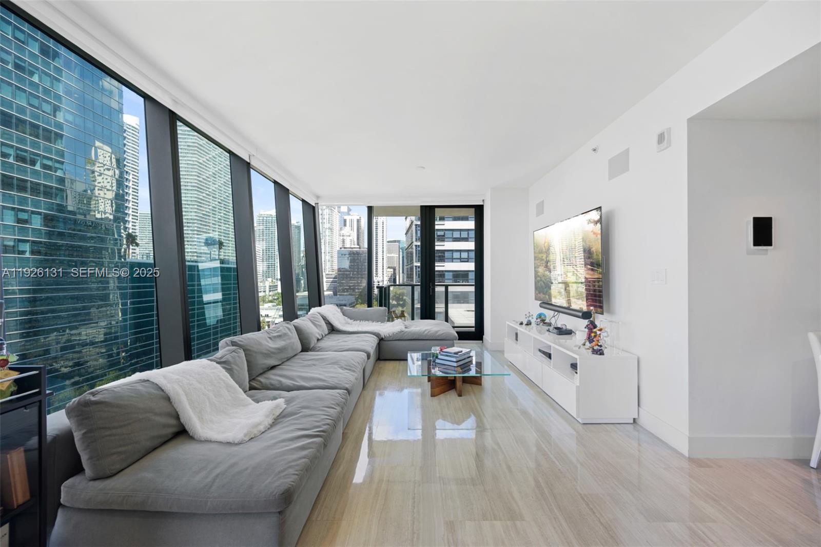 A modern living room features a large gray sectional sofa, glass coffee table, and floor-to-ceiling windows — 1451 Brickell Ave # 1106, Miami FL 33131, MIAMI, FL