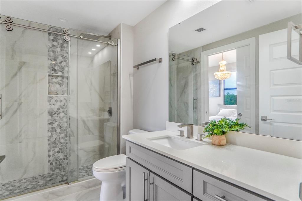 A modern bathroom features a glass-enclosed shower, a gray vanity, and a large wall mirror — 16300 COUNTY ROAD 455 UNIT 401, MONTVERDE, FL