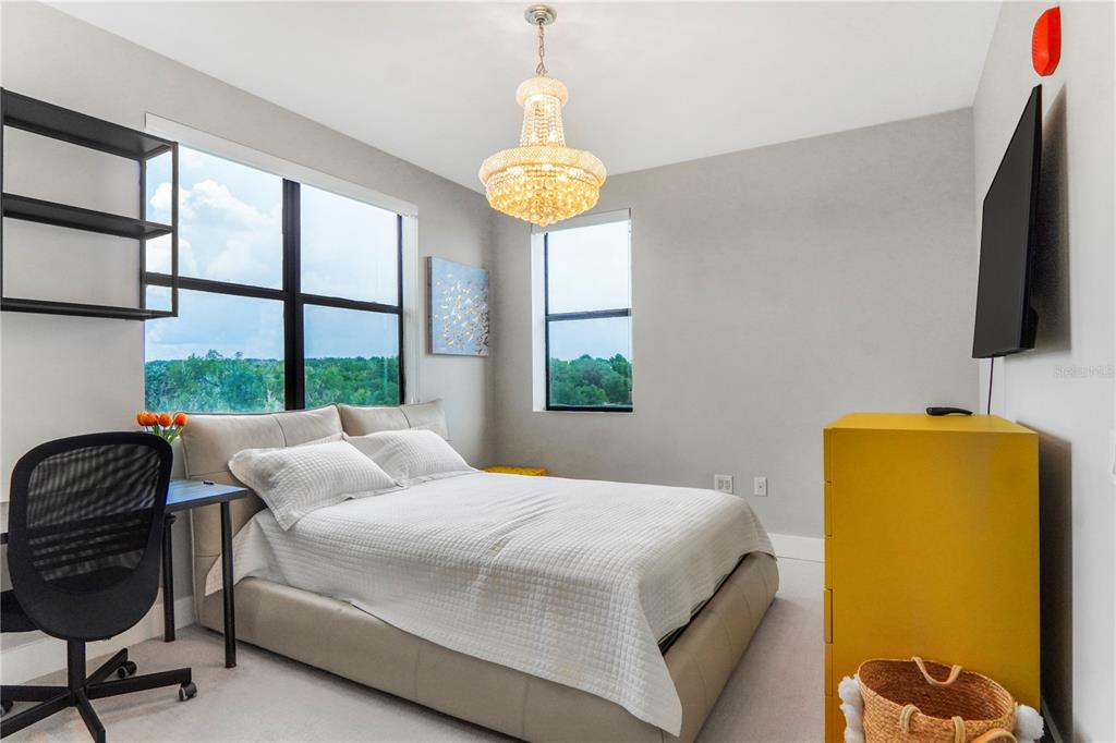 A bedroom features a bed, a desk with a chair, a yellow dresser, and a chandelier — 16300 COUNTY ROAD 455 UNIT 401, MONTVERDE, FL