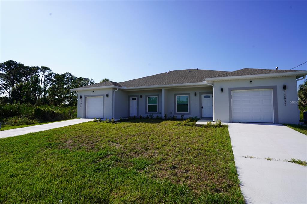 A single-story duplex with two garages, light gray siding, and a grassy front yard — 12030 TETZEL AVENUE, PORT CHARLOTTE, FL