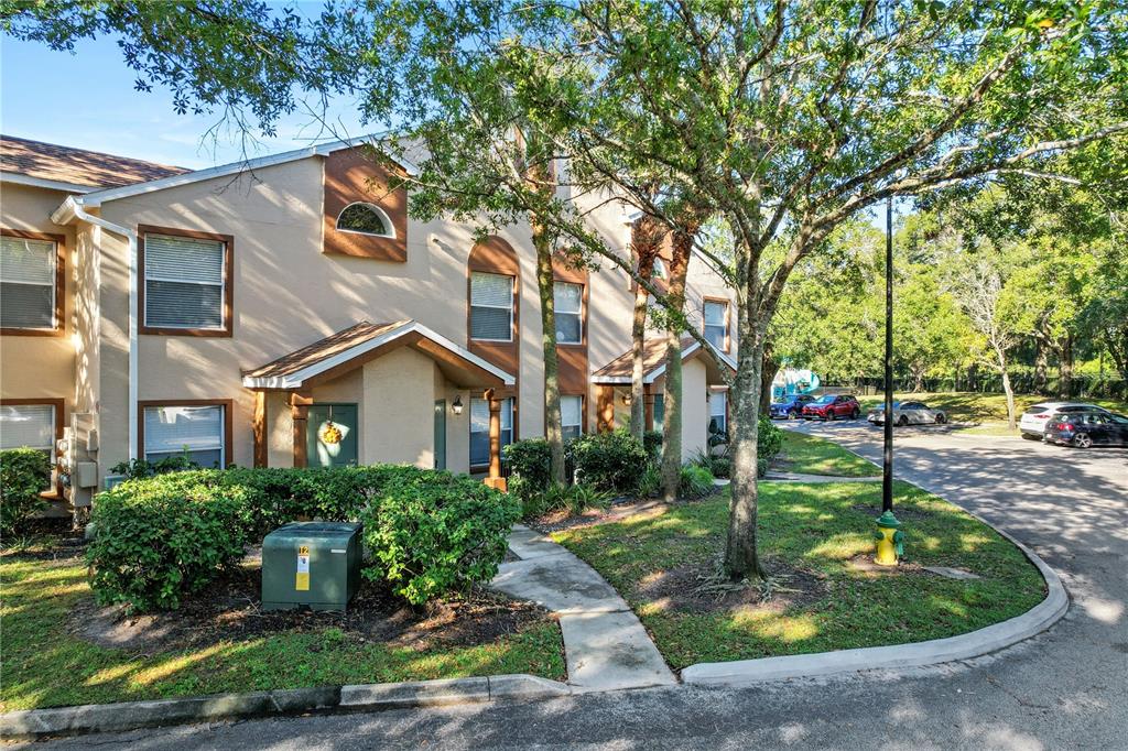 A two-story tan townhouse exterior with a green front door and surrounding landscaping — 5468 E MICHIGAN STREET UNIT 5468-4, ORLANDO, FL