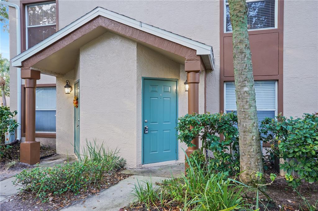 The exterior of a tan building features a teal front door under a covered entryway — 5468 E MICHIGAN STREET UNIT 5468-4, ORLANDO, FL