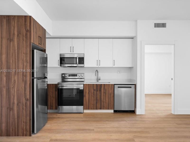 A modern kitchen features white upper cabinets, wood-grain lower cabinets, and stainless steel appliances — 2479 NE 192nd St # 306, Miami FL 33180, MIAMI, FL
