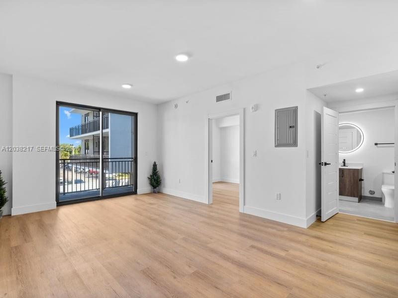 An empty room with light wood floors, white walls, a sliding glass door, and a bathroom — 2479 NE 192nd St # 306, Miami FL 33180, MIAMI, FL