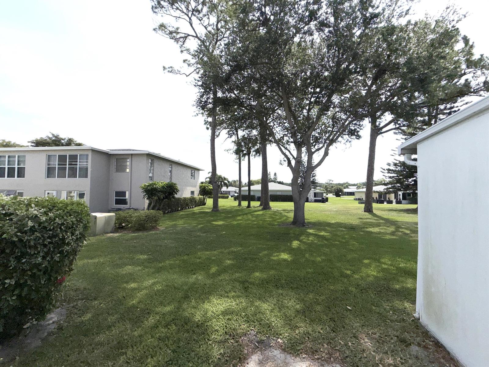 A grassy yard sits between a multi-story apartment building and a white exterior wall — 1030 Silk Oak Terrace # 101, Delray Beach FL 33445, DELRAY BEACH, FL
