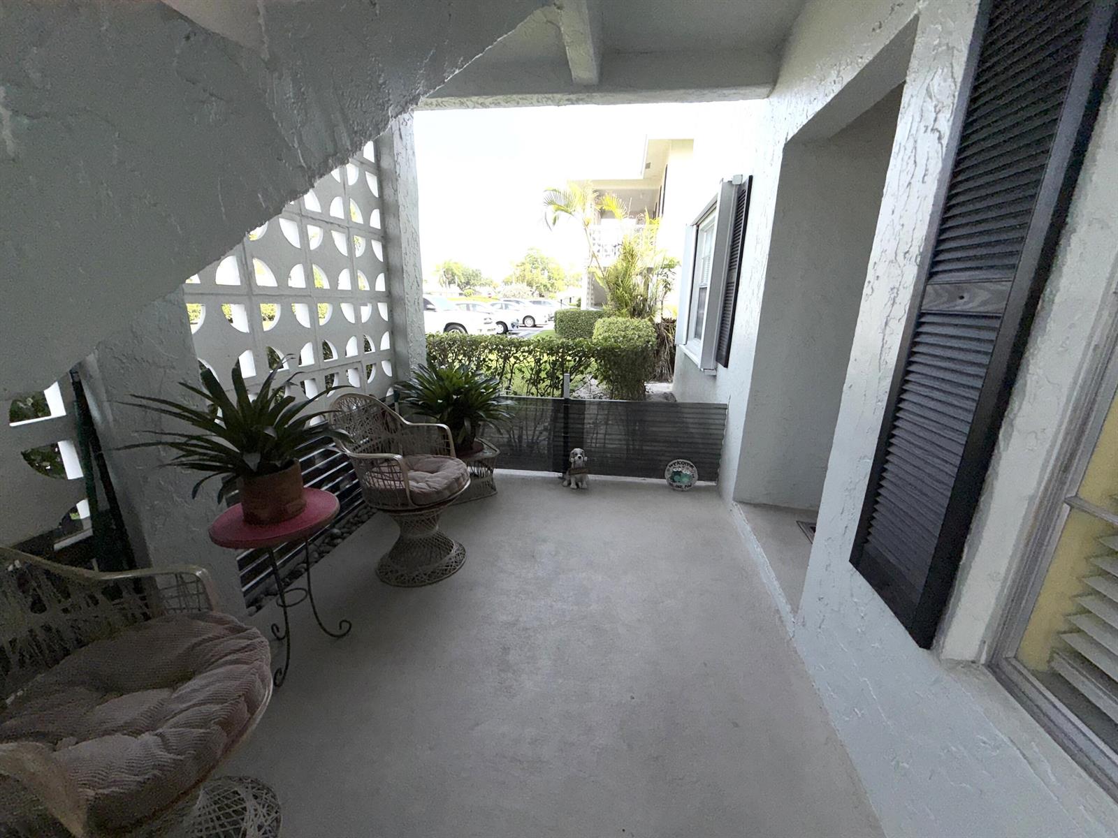 A covered patio features white concrete walls, decorative breeze blocks, wicker furniture, and potted plants — 1030 Silk Oak Terrace # 101, Delray Beach FL 33445, DELRAY BEACH, FL