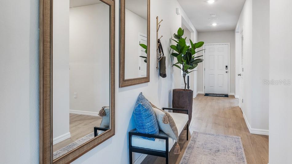 A bright entryway features a bench, mirrors, a potted plant, and light wood flooring — 17612 WHISKEY CREEK TRAIL, PARRISH, FL