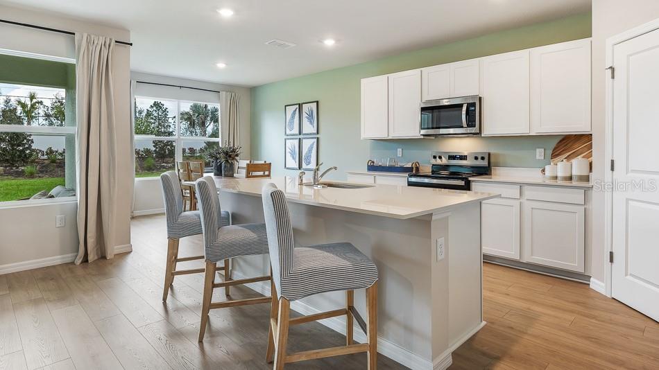 A kitchen features white cabinets, a quartz island with bar stools, and light wood flooring — 17612 WHISKEY CREEK TRAIL, PARRISH, FL
