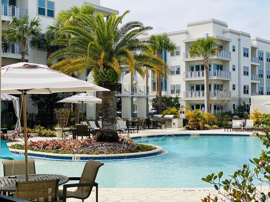 A swimming pool with a central palm tree island sits before a multi-story apartment building — 1688 CELEBRATION BOULEVARD UNIT The Sunset, CELEBRATION, FL