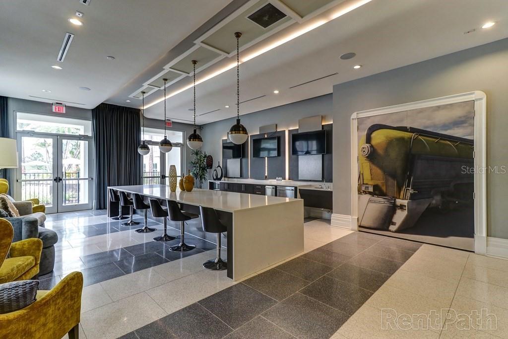 A modern lounge area features a long kitchen island, bar stools, and a large train mural — 1688 CELEBRATION BOULEVARD UNIT The Sunset, CELEBRATION, FL