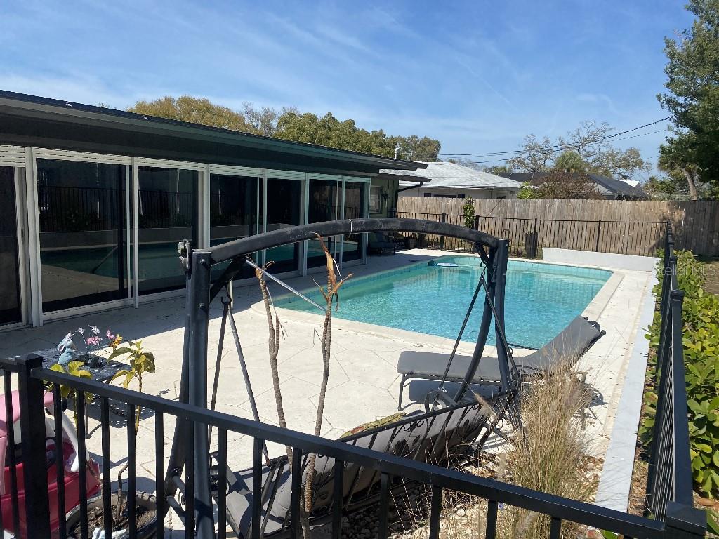 A backyard features a rectangular swimming pool, a patio, and a black metal swing set — 307 ORANGEWOOD LANE, LARGO, FL