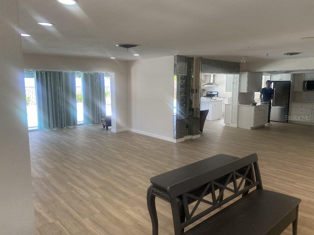 An open-concept living area with light wood-look flooring leads to a kitchen with white cabinetry — 307 ORANGEWOOD LANE, LARGO, FL