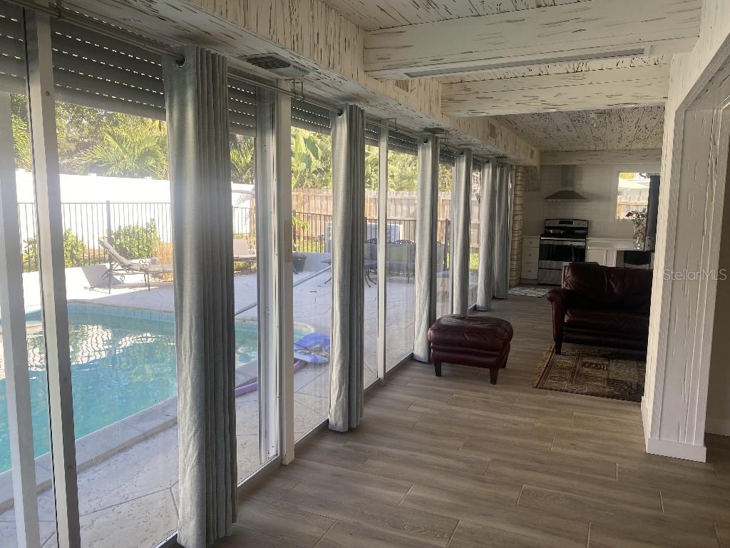 A sunroom with wood-look tile floors and a pool view opens into a kitchen area — 307 ORANGEWOOD LANE, LARGO, FL