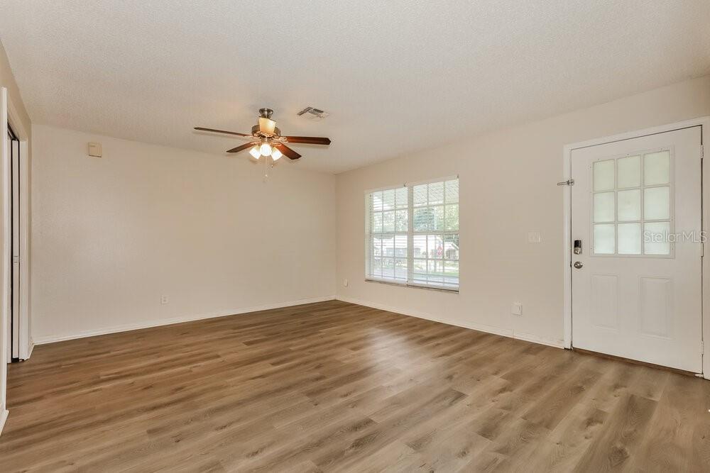 An empty living room with light wood-look flooring, a ceiling fan, and a white door — 37340 CARTER AVENUE, DADE CITY, FL