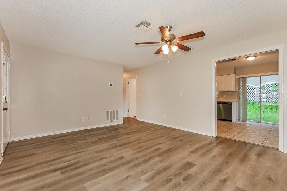 An empty living room with wood-look flooring, a ceiling fan, and an adjacent tiled kitchen — 37340 CARTER AVENUE, DADE CITY, FL