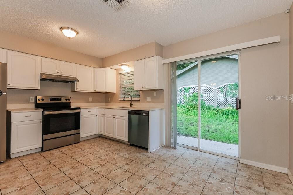 A kitchen with white cabinets, stainless steel appliances, tile flooring, and a sliding glass door — 37340 CARTER AVENUE, DADE CITY, FL