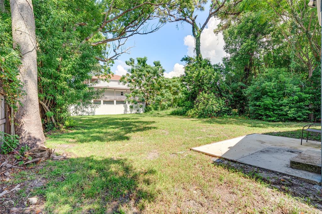 A grassy backyard features a concrete patio and dense trees surrounding a white fence — 7515 NEW YORK AVENUE, HUDSON, FL