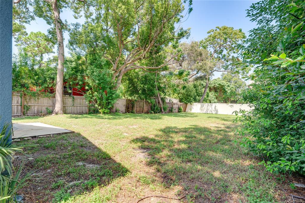 A grassy backyard features a concrete patio, mature trees, and a wooden privacy fence — 7515 NEW YORK AVENUE, HUDSON, FL