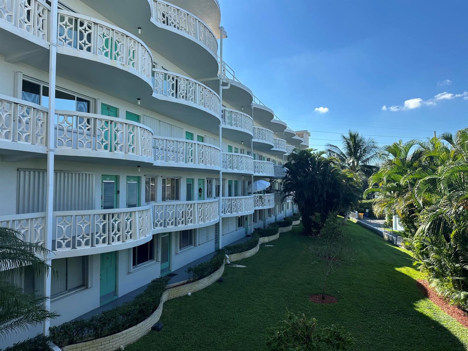 An exterior view of a multi-story apartment building with curved balconies and a grassy lawn — 2381 Sunset Avenue # 216, Lake Worth FL 33461, LAKE WORTH, FL