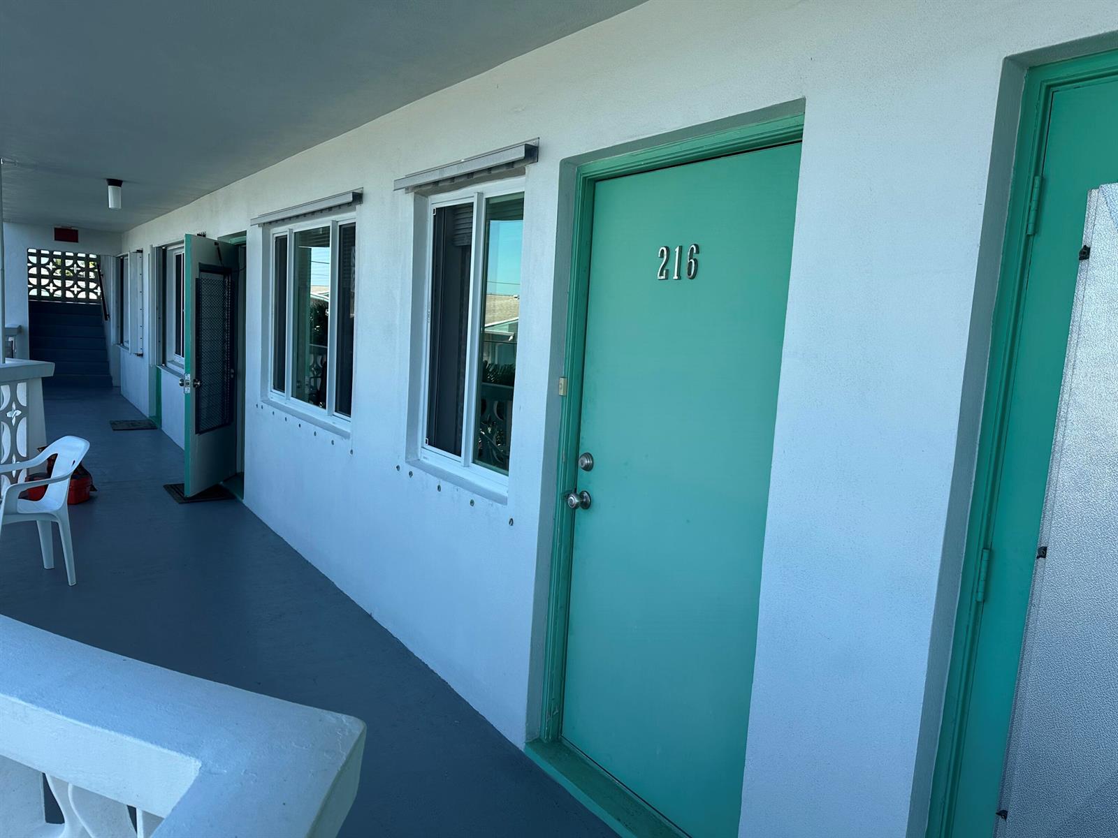 An exterior view of a motel walkway featuring teal doors and white walls — 2381 Sunset Avenue # 216, Lake Worth FL 33461, LAKE WORTH, FL