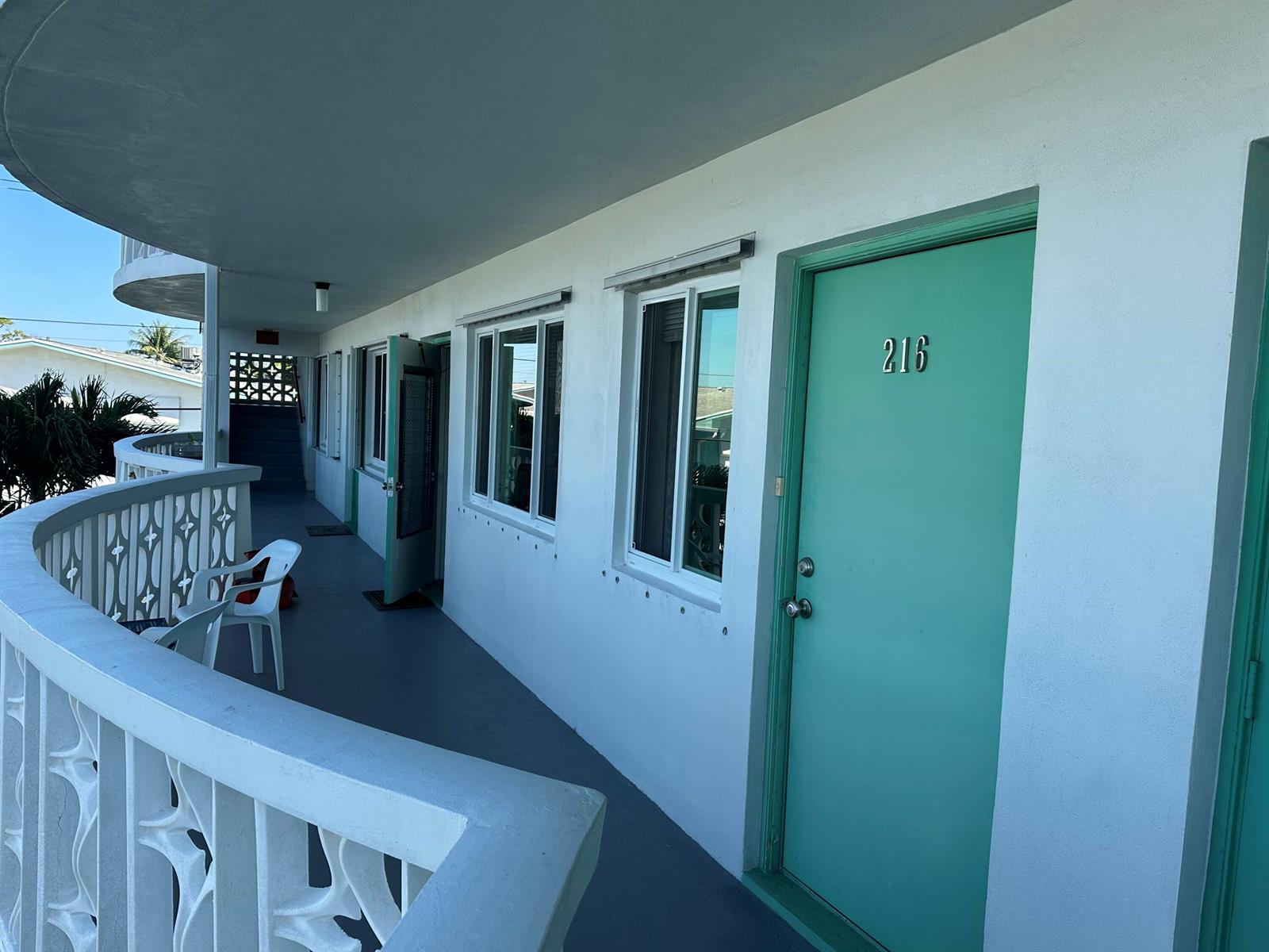 An exterior walkway with a white railing leads to a teal door numbered 216 — 2381 Sunset Avenue # 216, Lake Worth FL 33461, LAKE WORTH, FL
