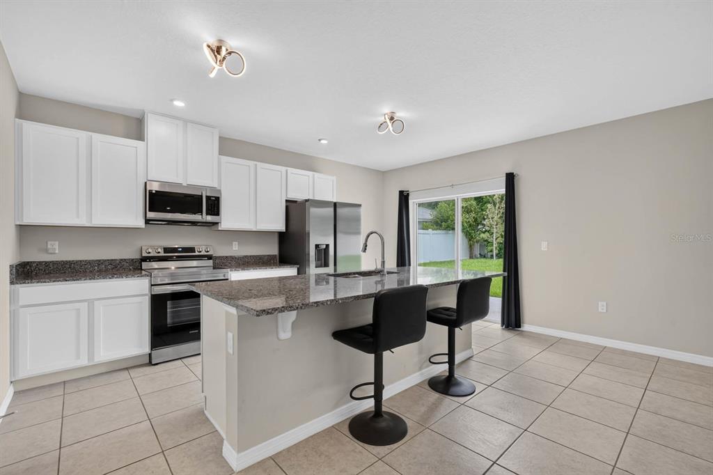 A kitchen features white cabinets, granite countertops, a stainless steel refrigerator, and a breakfast bar — 2323 FERN PALM DRIVE, EDGEWATER, FL