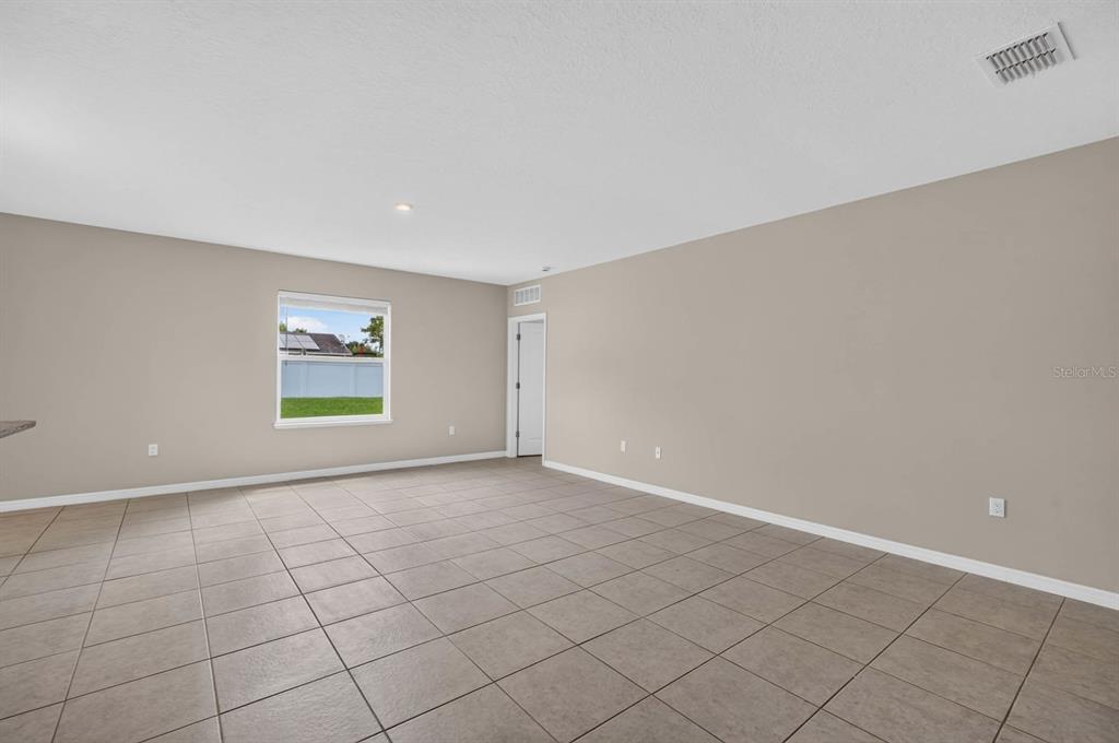 An empty room with beige walls, tile flooring, a window, and a white door — 2323 FERN PALM DRIVE, EDGEWATER, FL