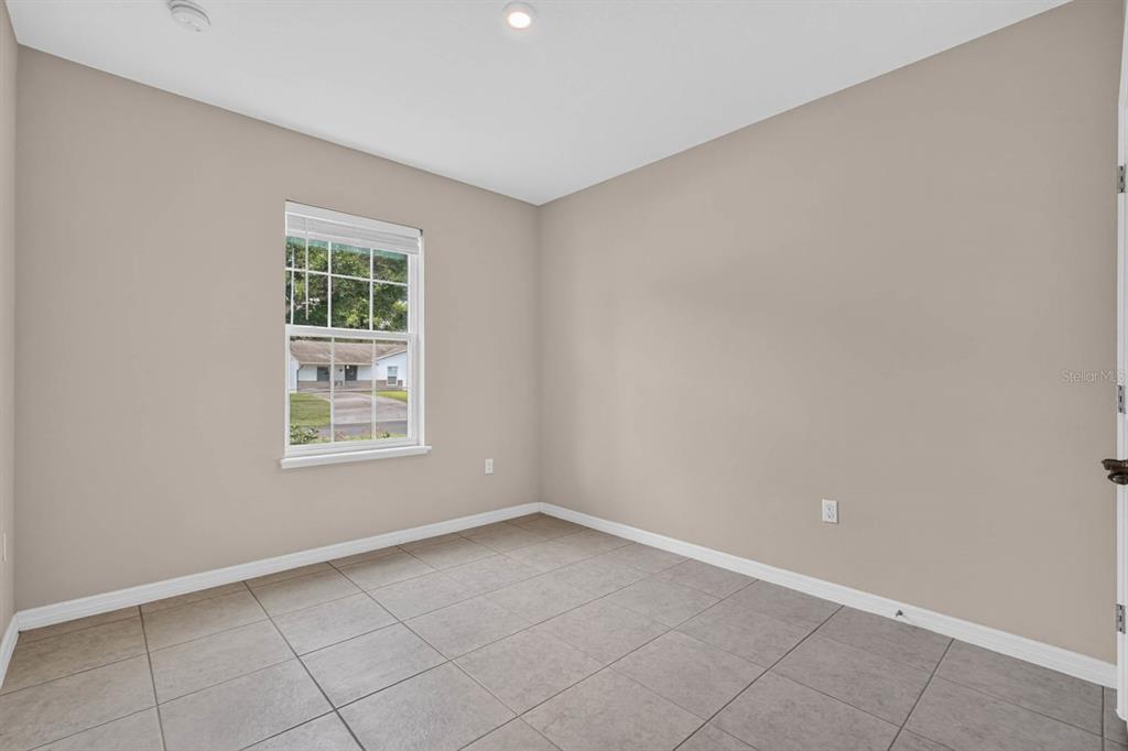 An empty room with beige walls, large square floor tiles, and a single window — 2323 FERN PALM DRIVE, EDGEWATER, FL