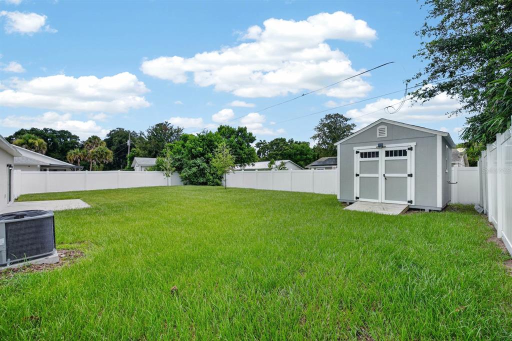 A backyard features a green lawn, a white vinyl fence, and a gray storage shed — 2323 FERN PALM DRIVE, EDGEWATER, FL
