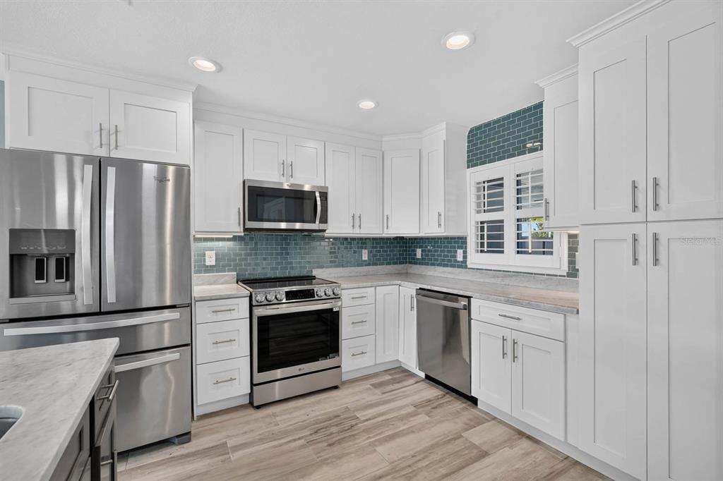 A kitchen with white cabinets, stainless steel appliances, a blue tile backsplash, and wood-look flooring — 1136 HARBOUR POINT DRIVE, PORT ORANGE, FL