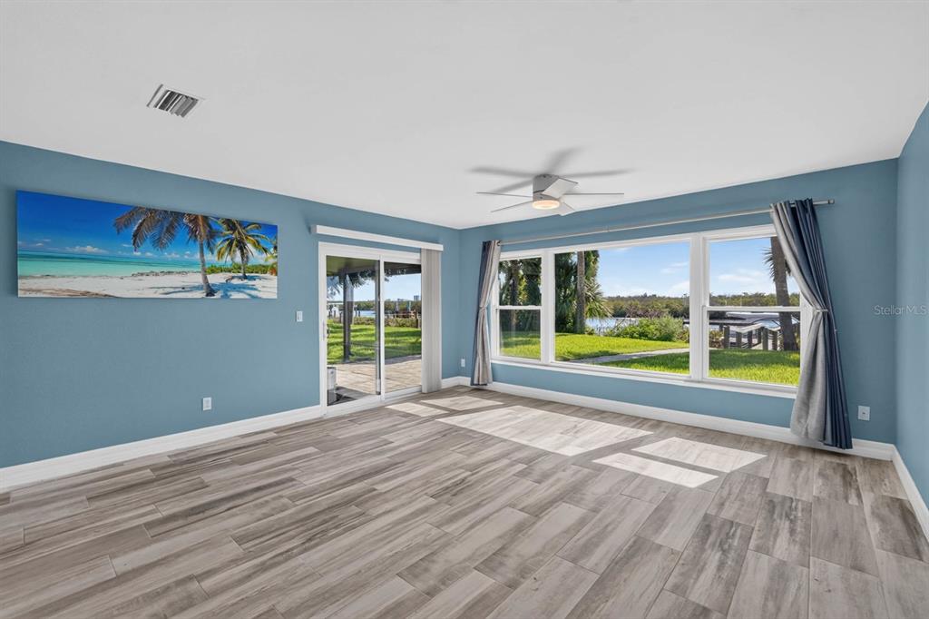 A living room with blue walls, wood-look tile flooring, a ceiling fan, and large windows — 1136 HARBOUR POINT DRIVE, PORT ORANGE, FL