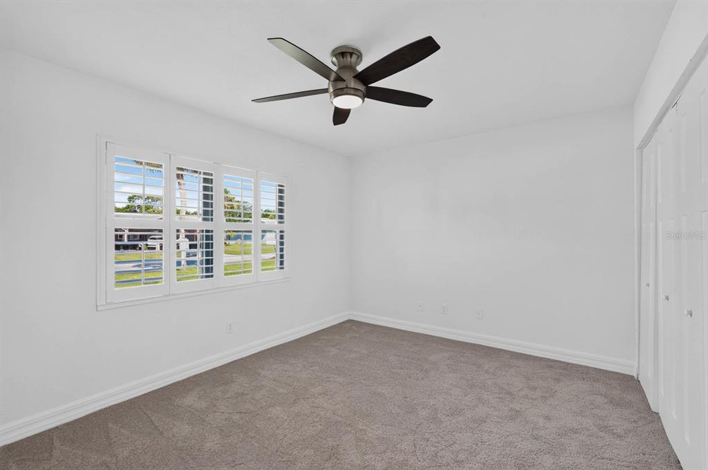 A bedroom with white walls, gray carpet, a ceiling fan, and plantation shutters on windows — 1136 HARBOUR POINT DRIVE, PORT ORANGE, FL
