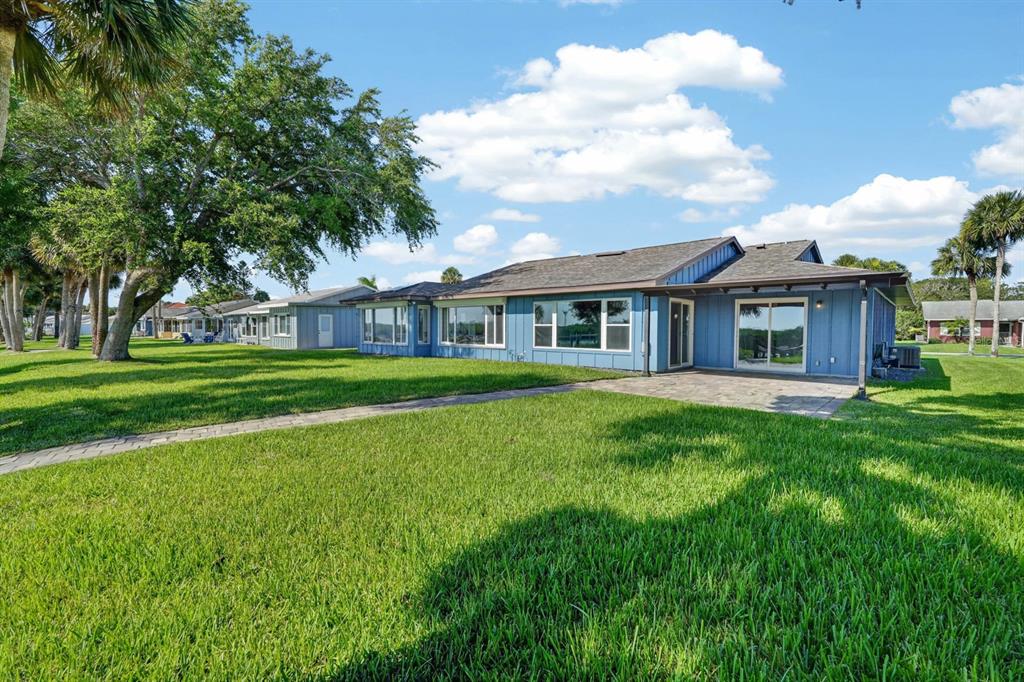A blue single-story house with a paved patio and large windows sits on a lawn — 1136 HARBOUR POINT DRIVE, PORT ORANGE, FL