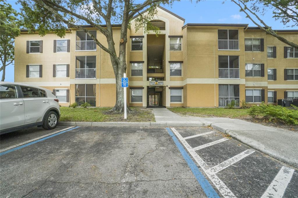 A three-story apartment building exterior features tan stucco walls, screened balconies, and a handicap parking space — 7524 SEURAT STREET UNIT 12301, ORLANDO, FL