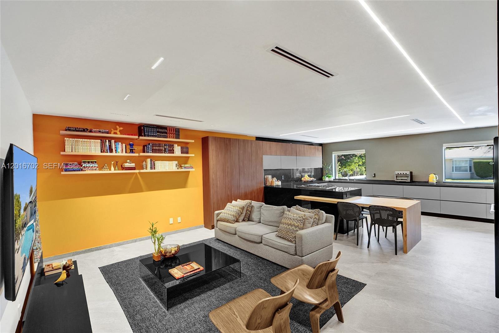 A modern open-concept living room and kitchen featuring an orange accent wall and wooden cabinetry — 19694 NE 24th Ave, Miami FL 33180, MIAMI, FL
