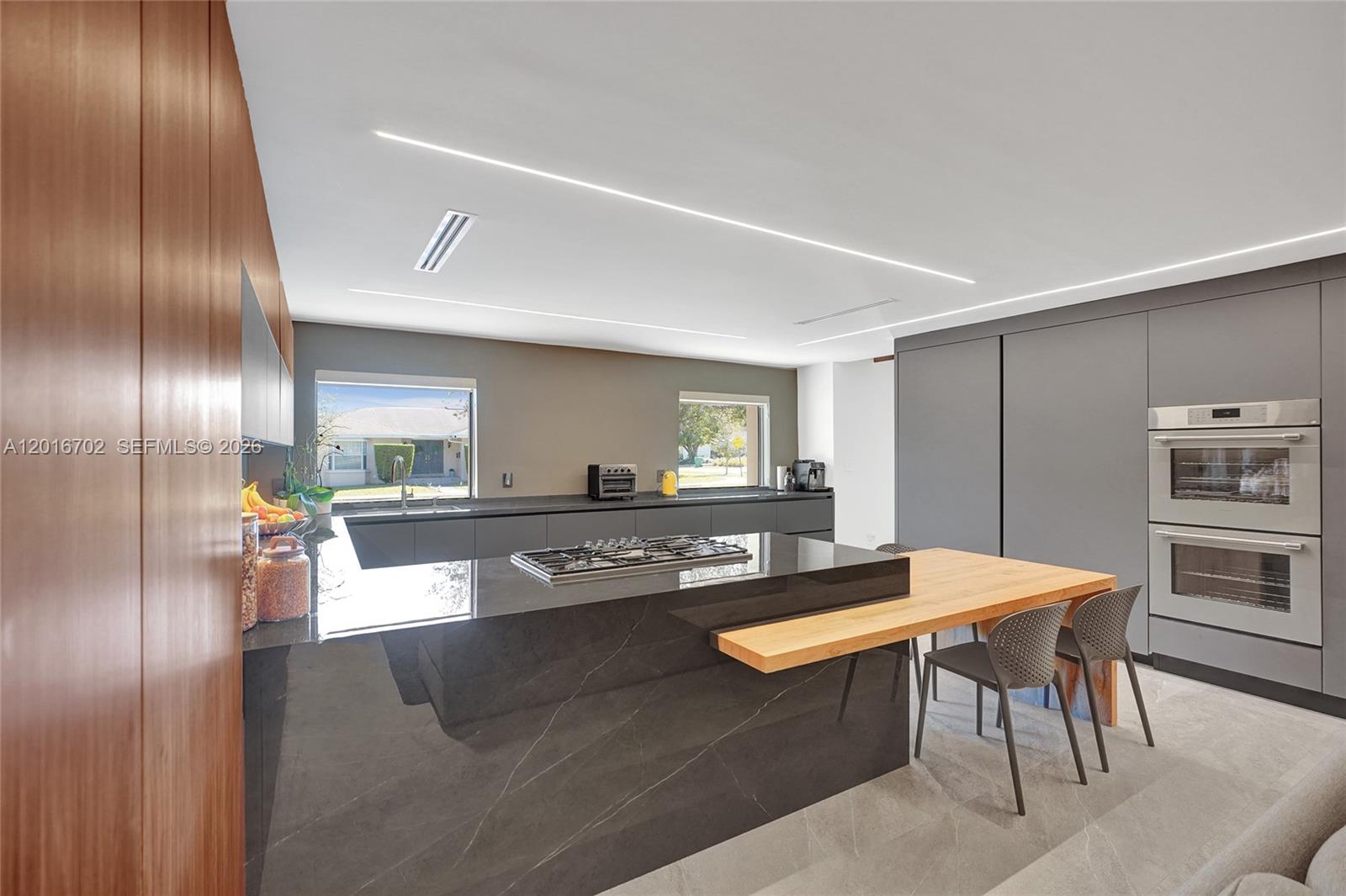 A modern kitchen features a dark stone island, integrated appliances, and a wooden dining extension — 19694 NE 24th Ave, Miami FL 33180, MIAMI, FL