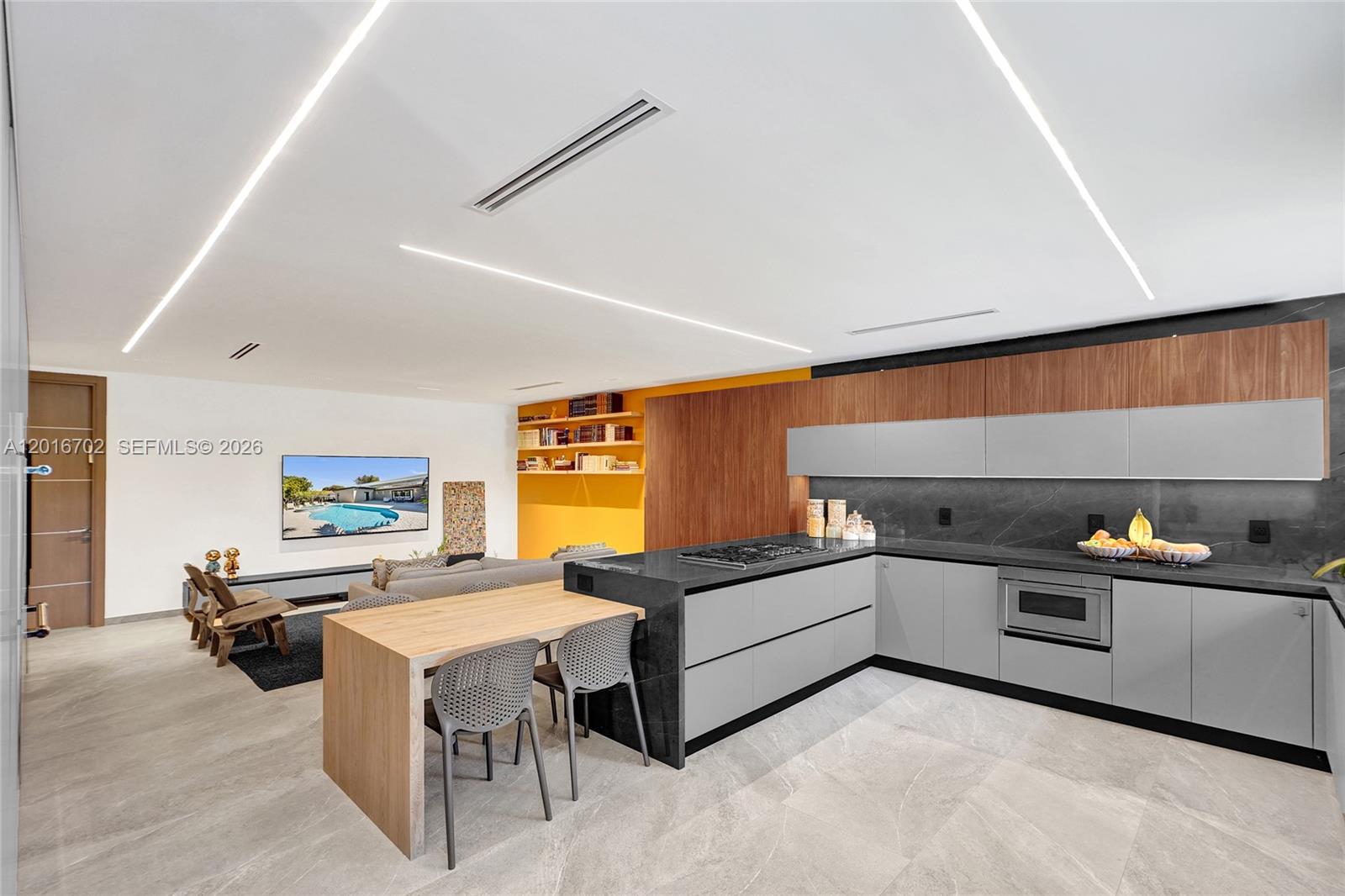 A modern kitchen features gray cabinetry, a black stone island, and an attached wooden table — 19694 NE 24th Ave, Miami FL 33180, MIAMI, FL