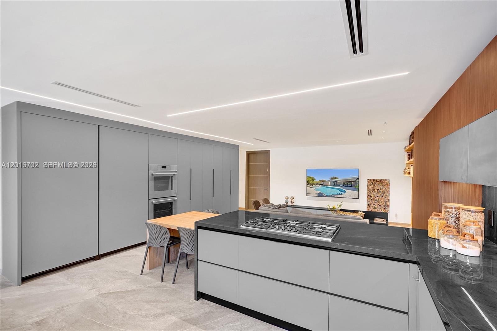 A modern kitchen features gray cabinetry, a black stone island with a cooktop, and dining area — 19694 NE 24th Ave, Miami FL 33180, MIAMI, FL