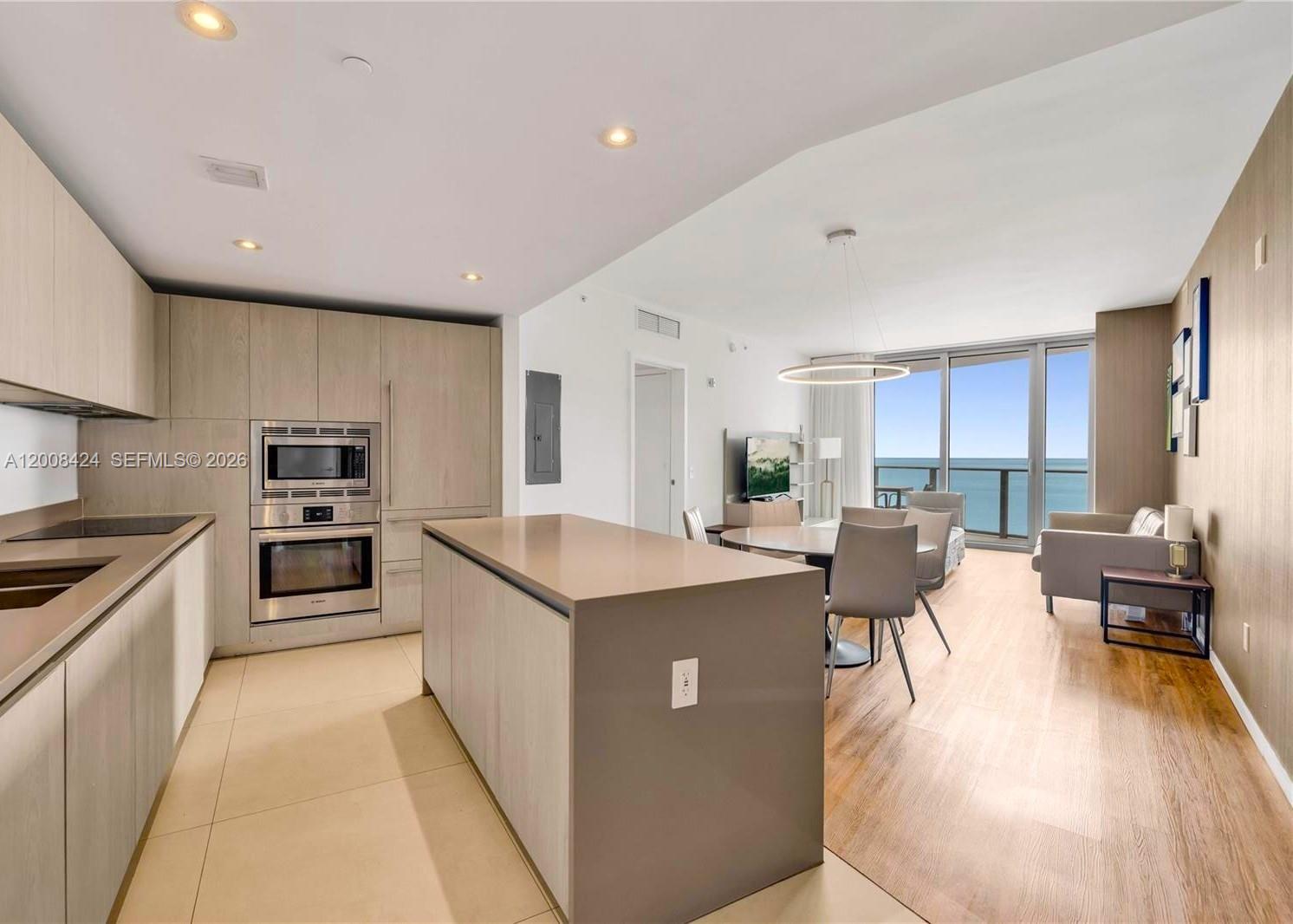 A modern kitchen with light wood cabinets and an island opens to a dining area — 4111 S Ocean Dr # 2303, Hollywood FL 33019, HOLLYWOOD, FL