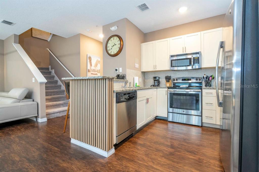 A kitchen with stainless steel appliances, white cabinets, and a slatted wood kitchen island — 2901 EDENSHIRE WAY UNIT 104, KISSIMMEE, FL