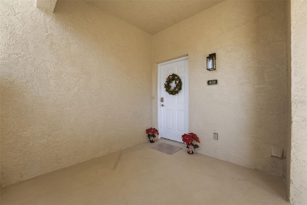 A covered entryway features a white front door with a wreath and two potted plants — 5800 SABAL TRACE DRIVE UNIT 401, NORTH PORT, FL