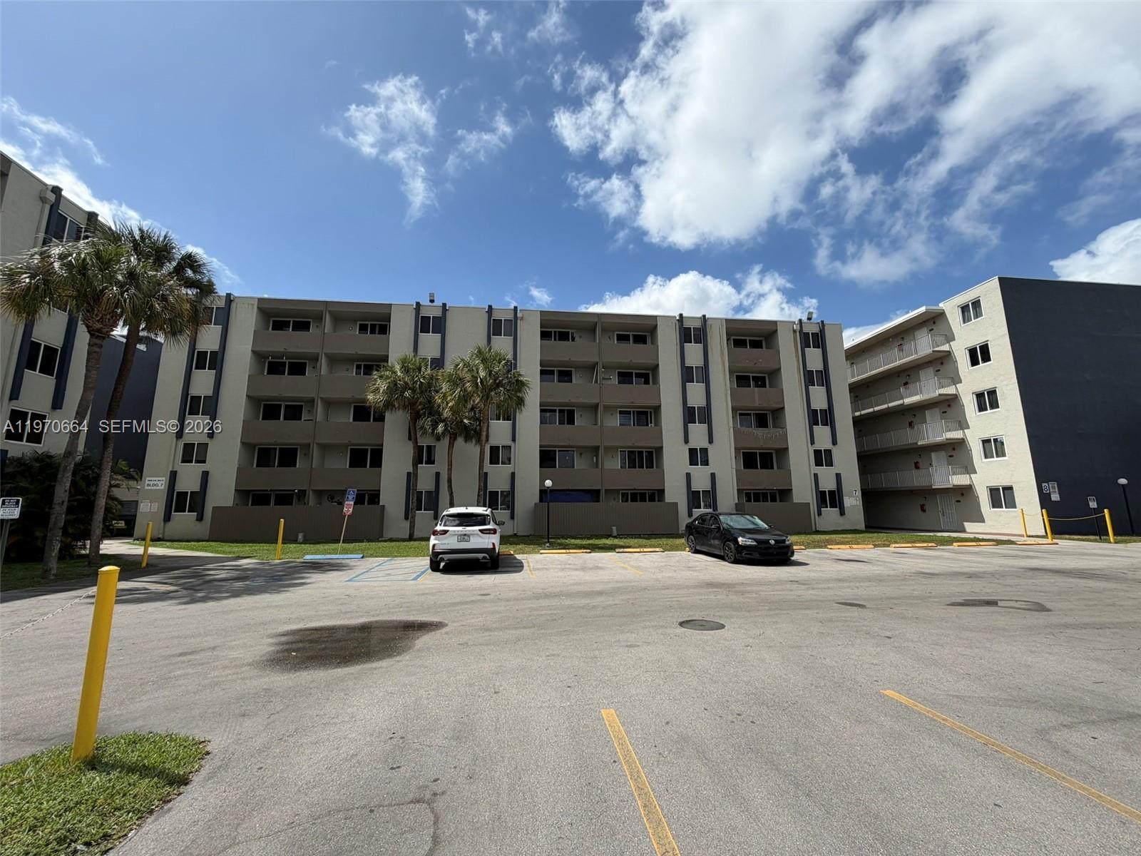 A multi-story apartment building features a parking lot with two cars in the foreground — 10090 NW 80th Ct # 1206, Hialeah Gardens FL 33016, HIALEAH GARDENS, FL