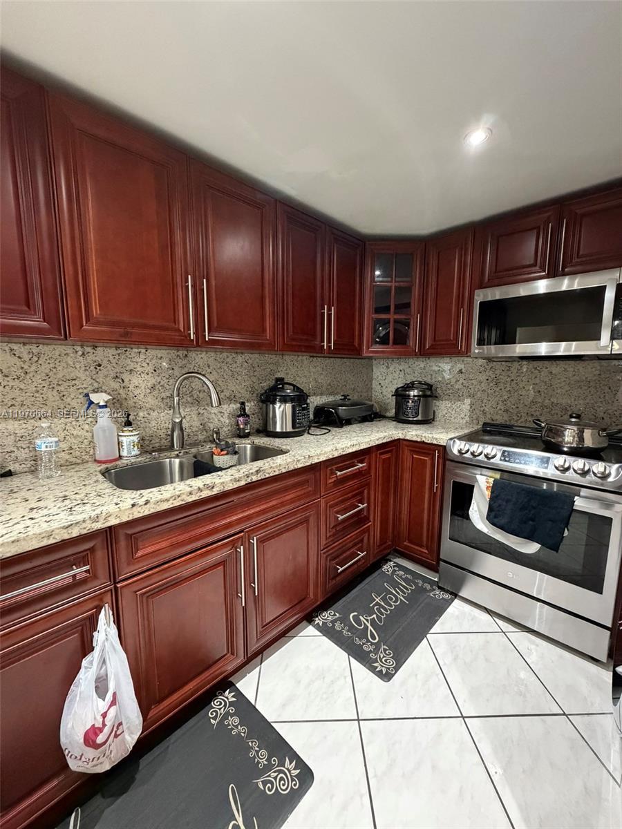 A kitchen features cherry wood cabinets, granite countertops, stainless steel appliances, and tiled floors — 10090 NW 80th Ct # 1206, Hialeah Gardens FL 33016, HIALEAH GARDENS, FL