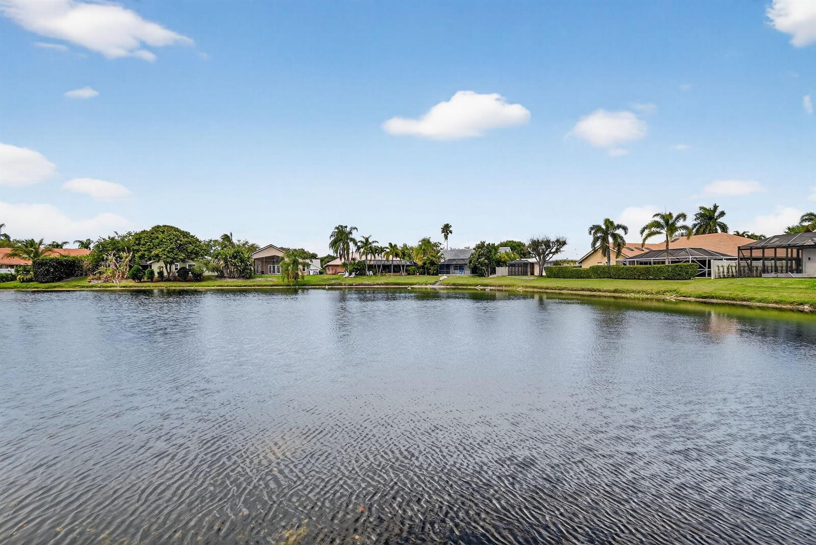 A view of a lake bordered by residential houses and palm trees under a blue sky — 2453 Stonegate Drive, Wellington FL 33414, WELLINGTON, FL