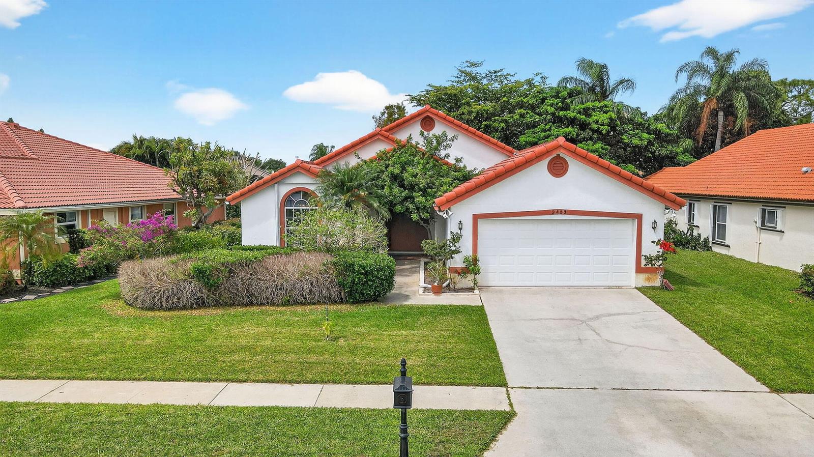 An aerial view shows three suburban houses with orange tile roofs near a lake — 2453 Stonegate Drive, Wellington FL 33414, WELLINGTON, FL