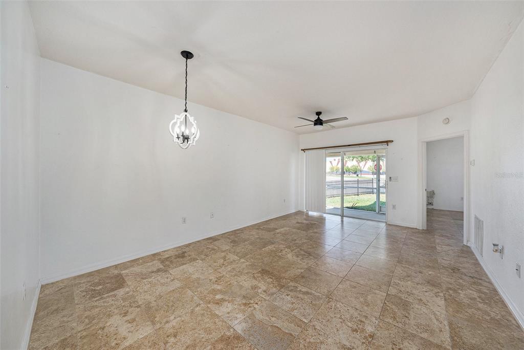 An empty room with tan tile flooring, a white chandelier, and a sliding glass door — 6011 SKYDALE WAY UNIT 101, RIVERVIEW, FL