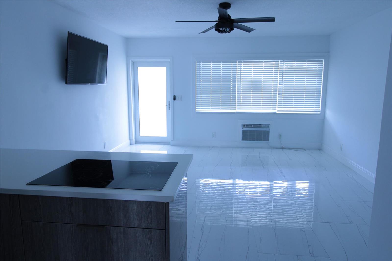 A kitchen island with a cooktop overlooks a bright living area with white tile floors — 600 Layne Boulevard # 119, Hallandale Beach FL 33009, HALLANDALE BEACH, FL